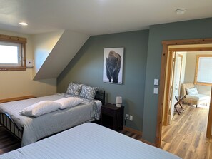 Een slaapkamer met twee bedden, een nachtkastje, een lamp, een aan de muur hangend schilderij en een deur naar een andere kamer.