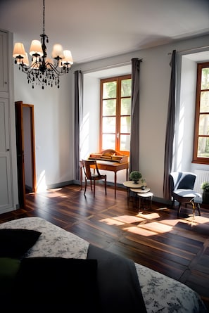 A room with a wooden floor, a chandelier, a dining table with chairs, a blue armchair, and large windows with curtains. - Large Charming House La Rivière, Heated Pool, Sleeps 15 (Calvignac)