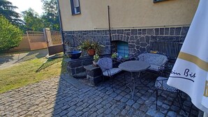 An outdoor patio with stone flooring, a stone wall, a fireplace, and patterned outdoor furniture. - Air-conditioned Holiday Apartment for up to 5 Guests in a Quiet Location near Eltz Castle (Naunheim)