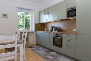 A kitchen with a window, a dining table with chairs, and a microwave.