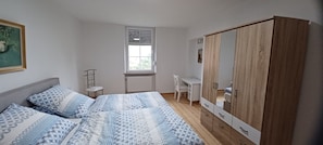 Quarto com cama, escrivaninha, guarda-roupa, janela e radiador.