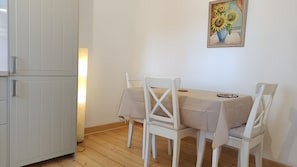 Uma sala de jantar com uma mesa e cadeiras, um frigorífico e um quadro na parede.