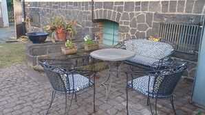 A patio with a stone wall, a metal table, and two patterned chairs.
