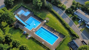 An aerial view of a property with two swimming pools, a covered patio area, and a solar panel-equipped building.