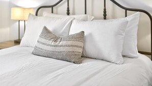 Ein Bett mit weißer Bettwäsche und zwei Kissen, eines gestreift, eines einfarbig, in einem Zimmer mit einem dunklen Metall-Kopfteil und einer Nachttischlampe.