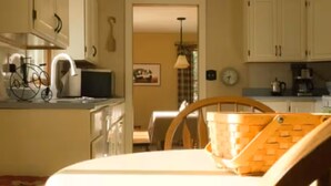 Una cucina con mobili bianchi, un tavolo da pranzo con sedie, un cesto sul tavolo e una sveglia appesa al muro.
