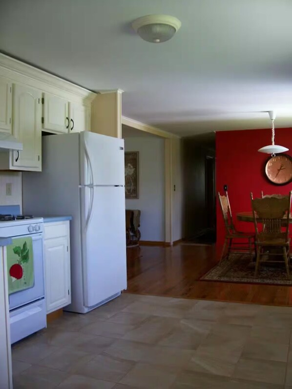 A kitchen with white cabinets, a refrigerator, and a stove. There is a dining area with a table and chairs.