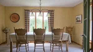 Una sala da pranzo con un tavolo, quattro sedie, un lampadario, un orologio e una finestra con tende.