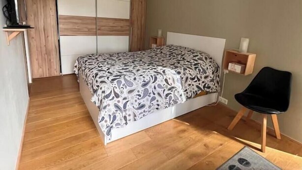 A bedroom with a bed, a wooden wardrobe, a small shelf, and a chair. - Architect-designed wooden house with breathtaking panoramic view of the Vilaine river (Nivillac)