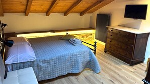 Une chambre à coucher comprenant un lit, une table de chevet, une commode et un téléviseur fixé au mur.
