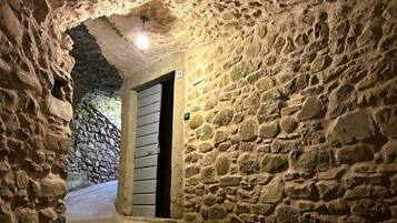 Un étroit couloir en pierre, avec une porte au bout, qui mène à un mur de pierre.
