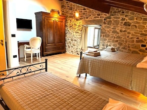 Une chambre avec deux lits, une armoire en bois, un bureau avec une chaise et un mur en pierre.