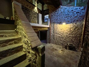 Un escalier en pierre mène à un balcon du deuxième étage, qui est bordé d’un mur en pierre et agrémenté d’un petit banc en bois.