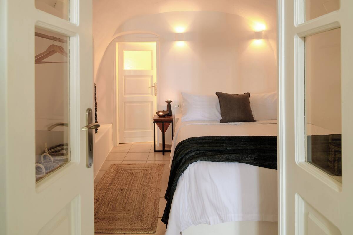 A bedroom with a bed, bedside table, and a door leading to a bathroom.