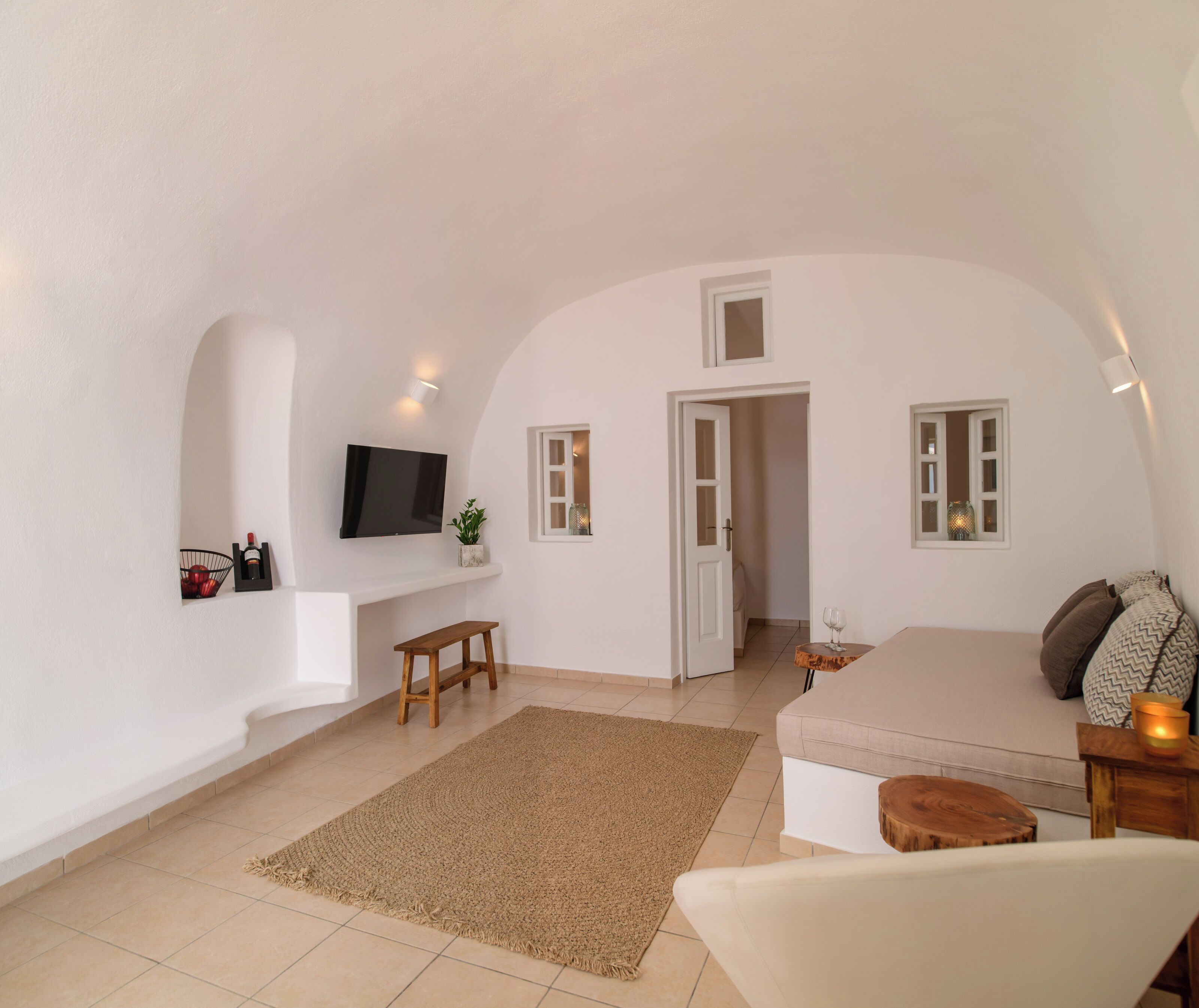 A spacious living area with a flat-screen TV, a bench, a sofa, and a small table with a candle.