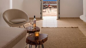 A room with a view of the sea, a sofa, a small table with a bottle and glasses, and a rug.
