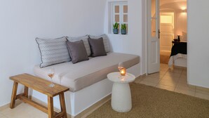 A cozy living room with a sofa, a small wooden table, a round side table with a candle, and a view into the adjacent room.