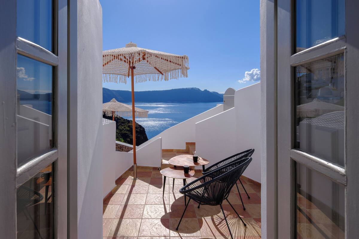 A balcony with a view of the sea, a table, two chairs, and a hanging white umbrella.