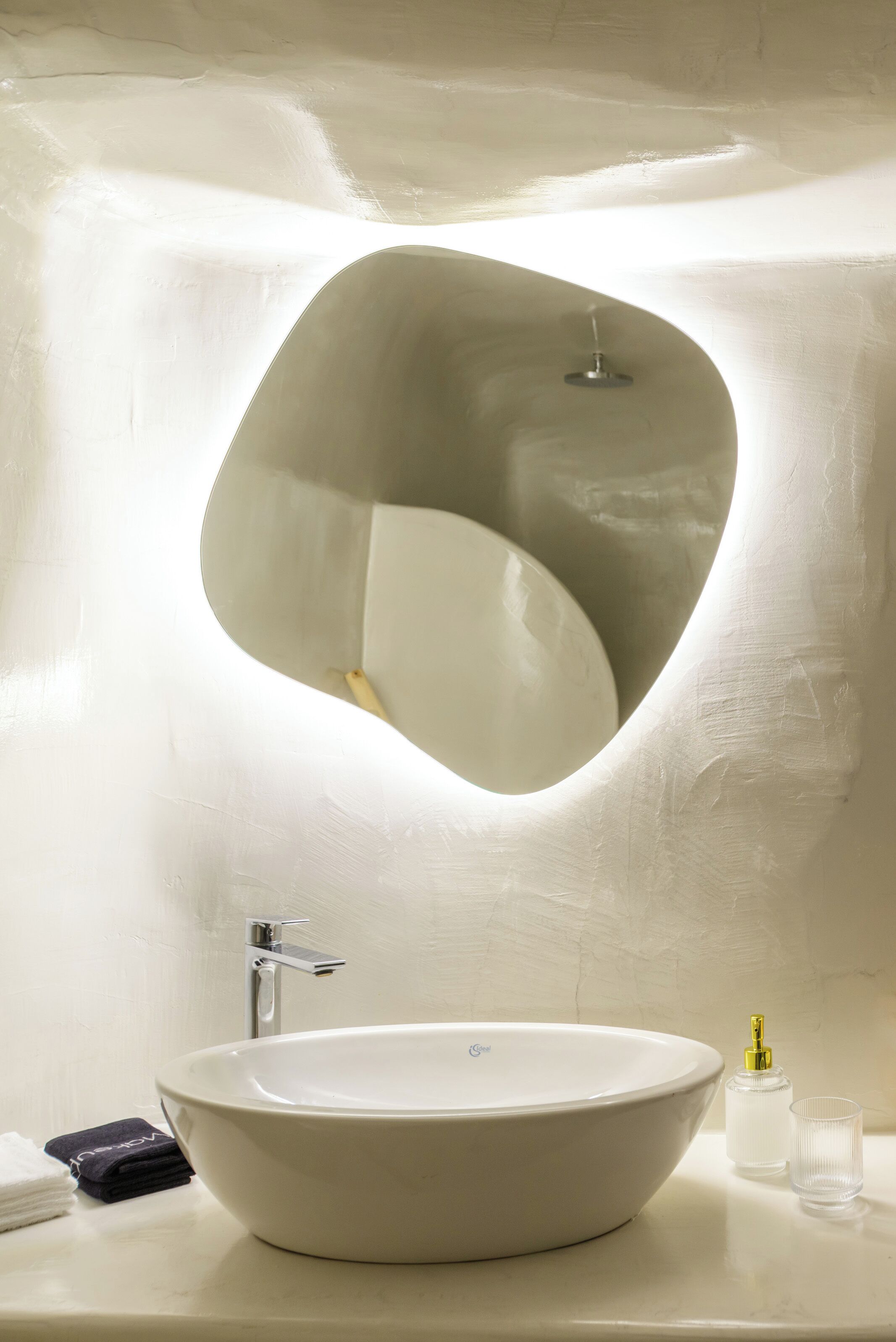 A modern bathroom with a large oval sink, a faucet, a soap dispenser, and a glass.