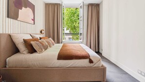 Un dormitorio con cama, ventana con cortinas, una obra de arte colgada en la pared y vista a zonas verdes afuera.