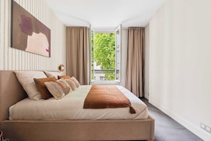 A bedroom with a bed, a window with curtains, a wall-mounted artwork, and a view of greenery outside. - Stylish Central and full of Light Loft - Paris 9th (Paris)