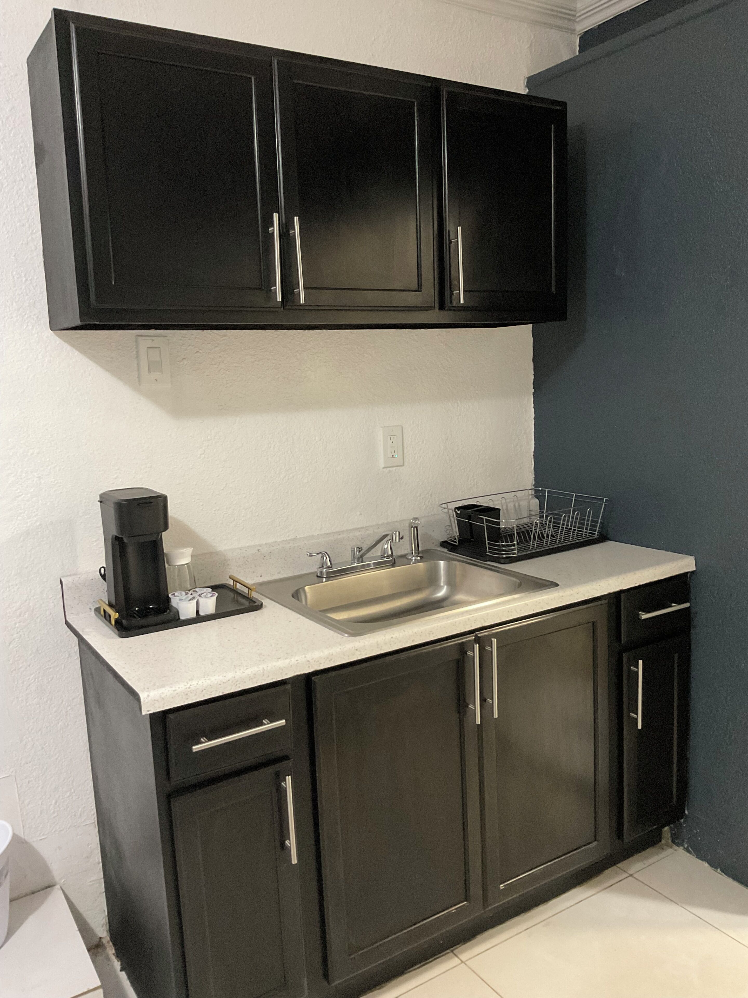 A kitchen with black cabinets, a stainless steel sink, and a coffee maker.