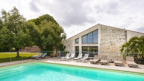 Un bâtiment moderne doté d’une piscine, de chaises longues et d’une façade en pierre.