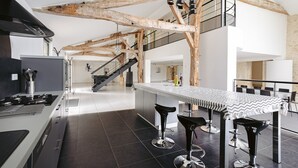 Une cuisine moderne dotée d’un îlot central, de tabourets de bar et de poutres apparentes.