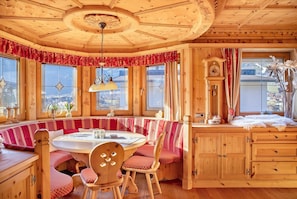 A wooden interior with a round table, bench seating, and a clock.