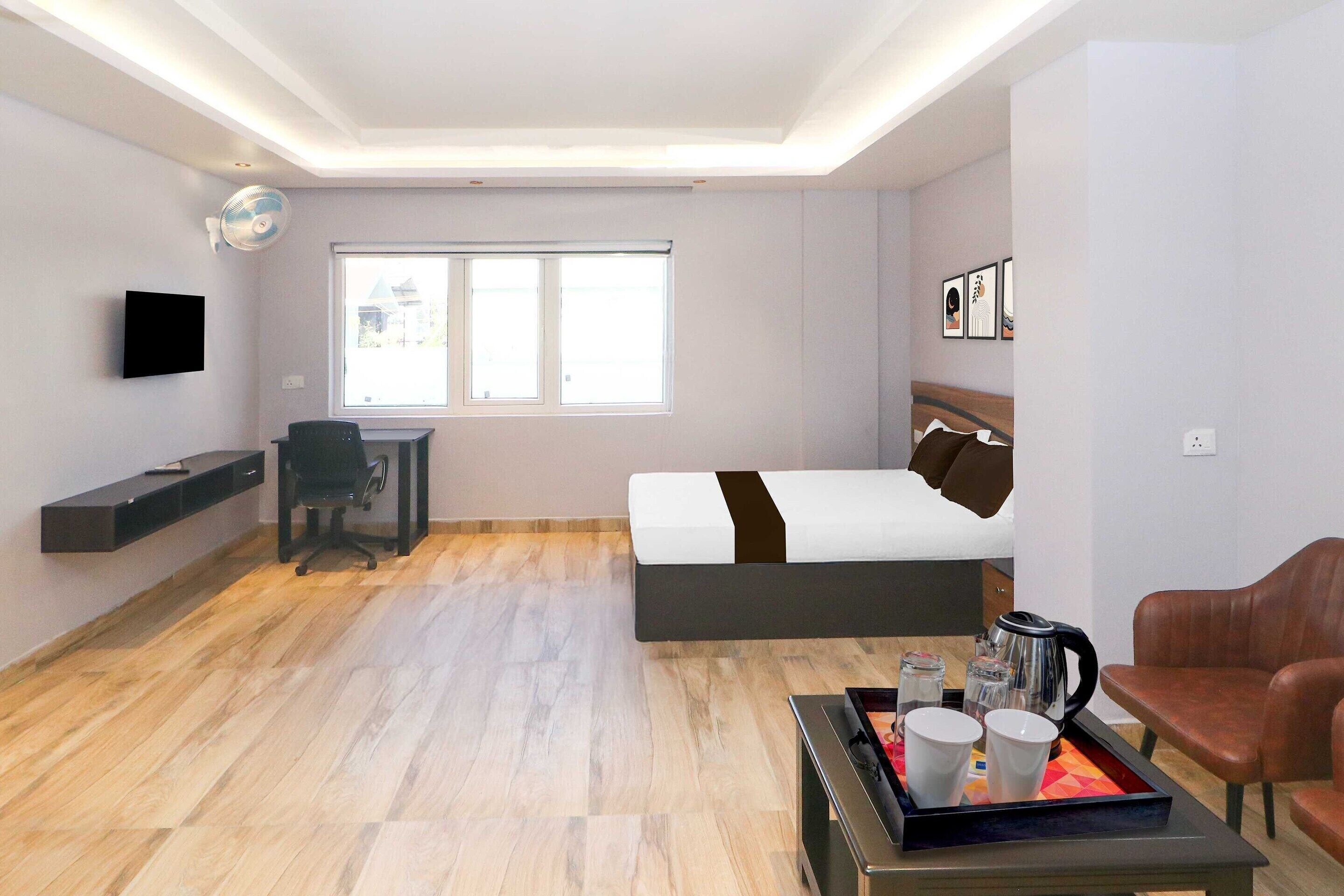 A hotel room with a bed, a desk, a chair, a coffee table with cups and a kettle, and a large window.