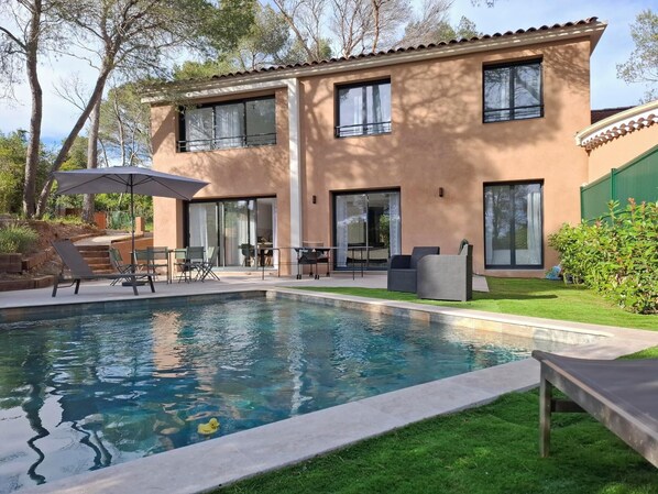A modern two-story house with a swimming pool, outdoor furniture, and a well-maintained lawn.