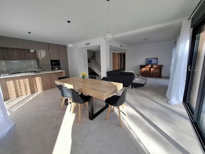 A modern kitchen with a dining area, a staircase, and a living room with a sofa and TV.