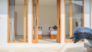 Habitación de hotel con puerta corrediza de vidrio, dos camas con ropa blanca y una gran escultura de un ave a la derecha.