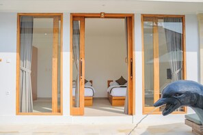 Habitación de hotel con puerta corrediza de vidrio, dos camas y una escultura de un pájaro.