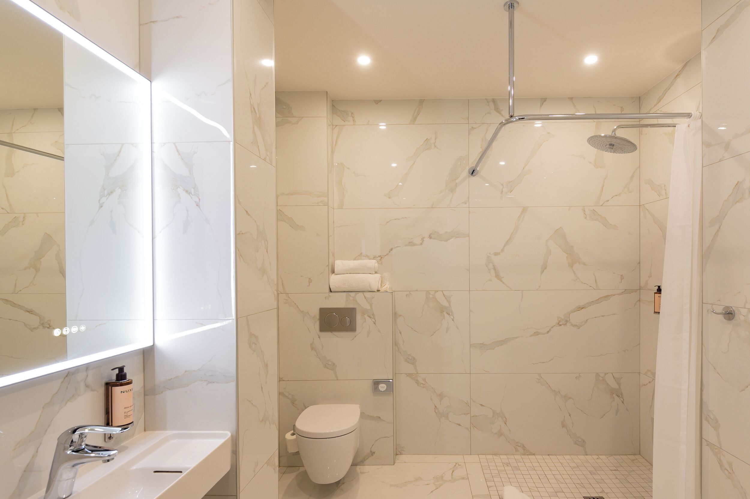 A modern bathroom with a marble floor, a toilet, a sink with a mirror, and a shower area.
