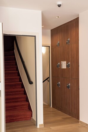 Eine Treppe mit rotem Teppich führt zu einem Raum, an der Wand sind Holzpaneele angebracht und eine Tür besitzt einen Lichtschalter.