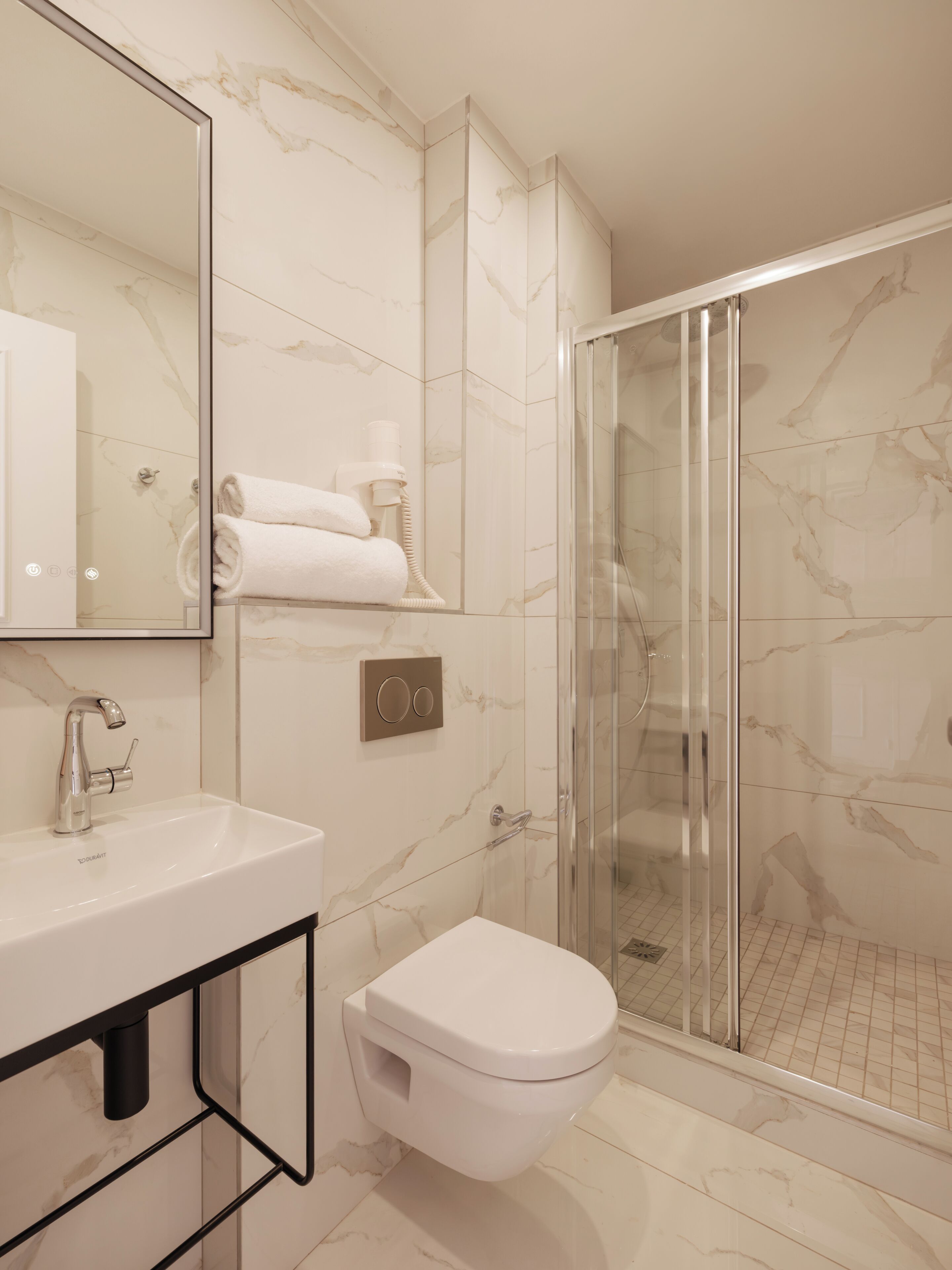 Un baño moderno con cabina de ducha de vidrio, inodoro blanco y pared revestida de mármol.