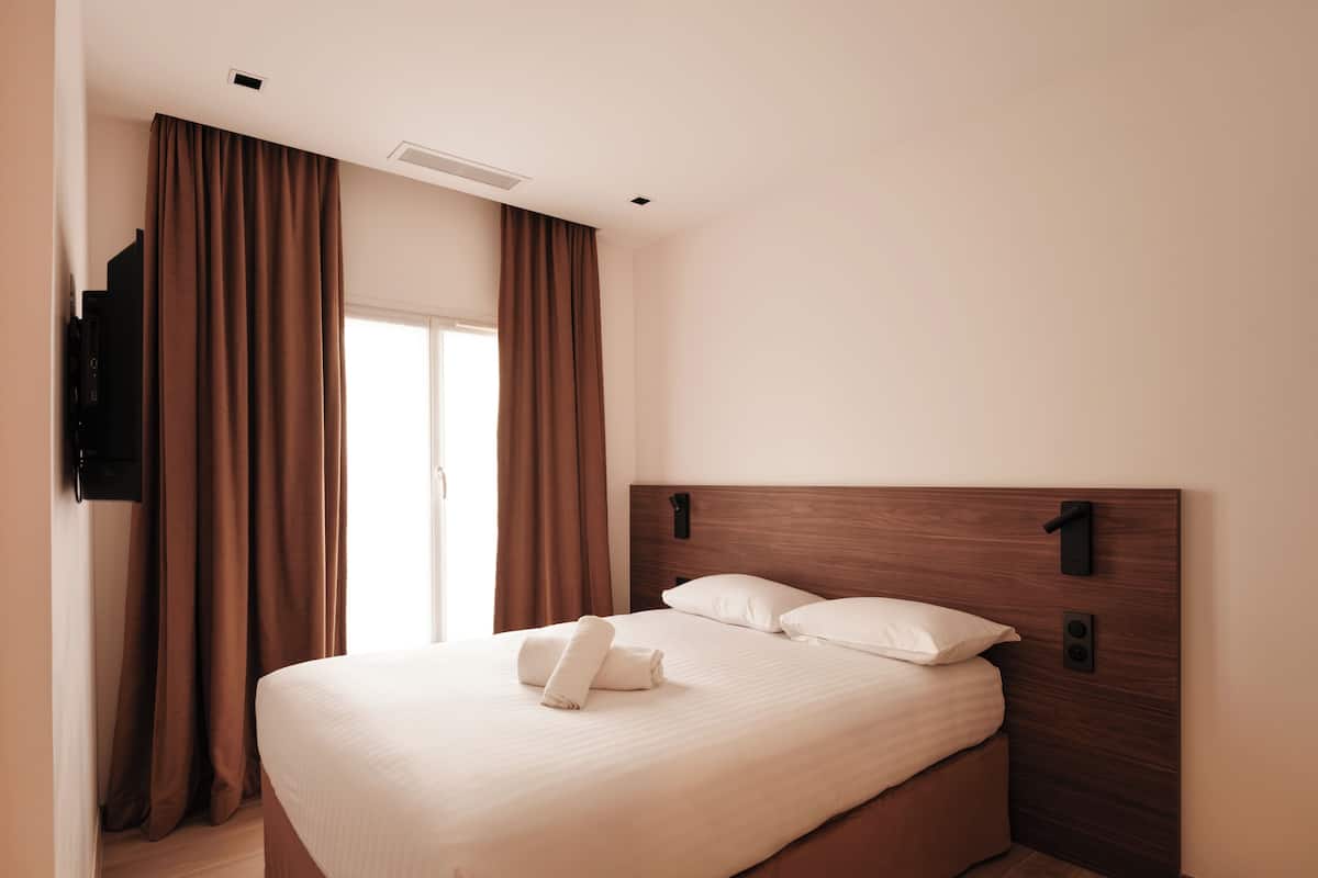 Ein Hotelzimmer mit einem großen Bett, braunen Vorhängen, einem Holz-Kopfteil und einem flachbildfernseher an der Wand.