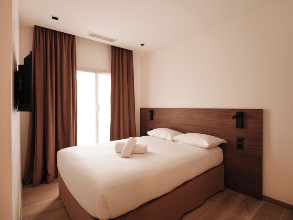 A hotel room with a large bed, brown curtains, a wooden headboard, and a flat-screen TV mounted on the wall. - Hotel Au Coeur du Haut Marais (Paris)