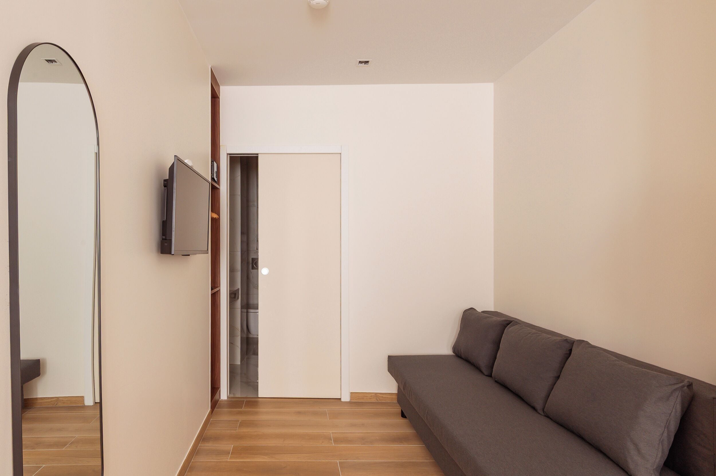 A modern living room with a sofa, a television, and a door leading to a bathroom.