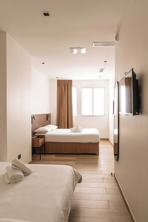 Ein Hotelzimmer mit zwei Betten, einem Fernseher, einem Schreibtisch und einem Fenster mit Vorhängen.