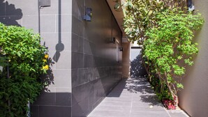 A narrow, tiled corridor with a wall-mounted light fixture, a door at the end, and greenery on the sides. - Darent Royal Threebedroom Al Malqa (Riyadh)