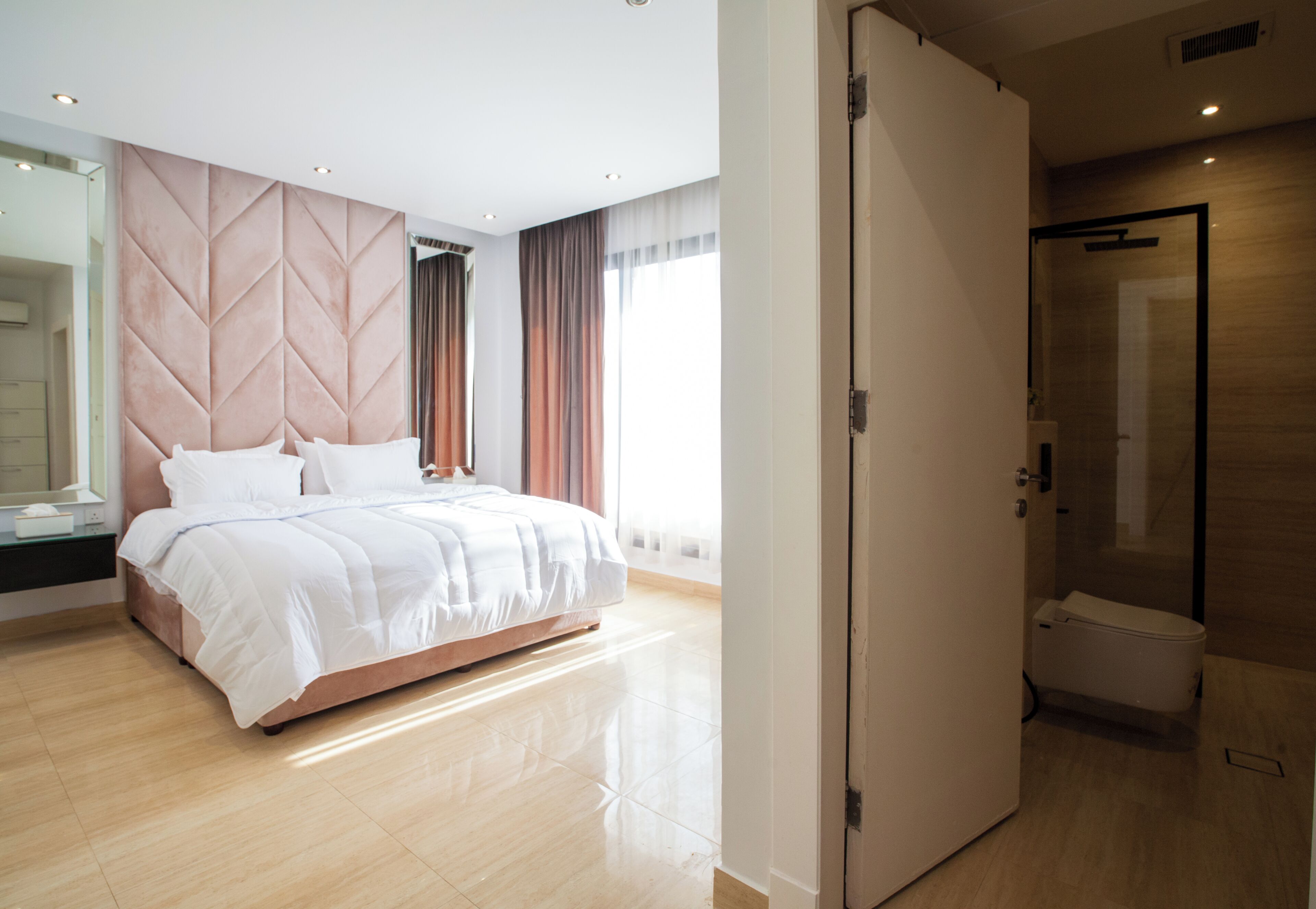 A modern hotel room with a large bed, a walk-in closet, a bathroom with a glass shower, and a large window.