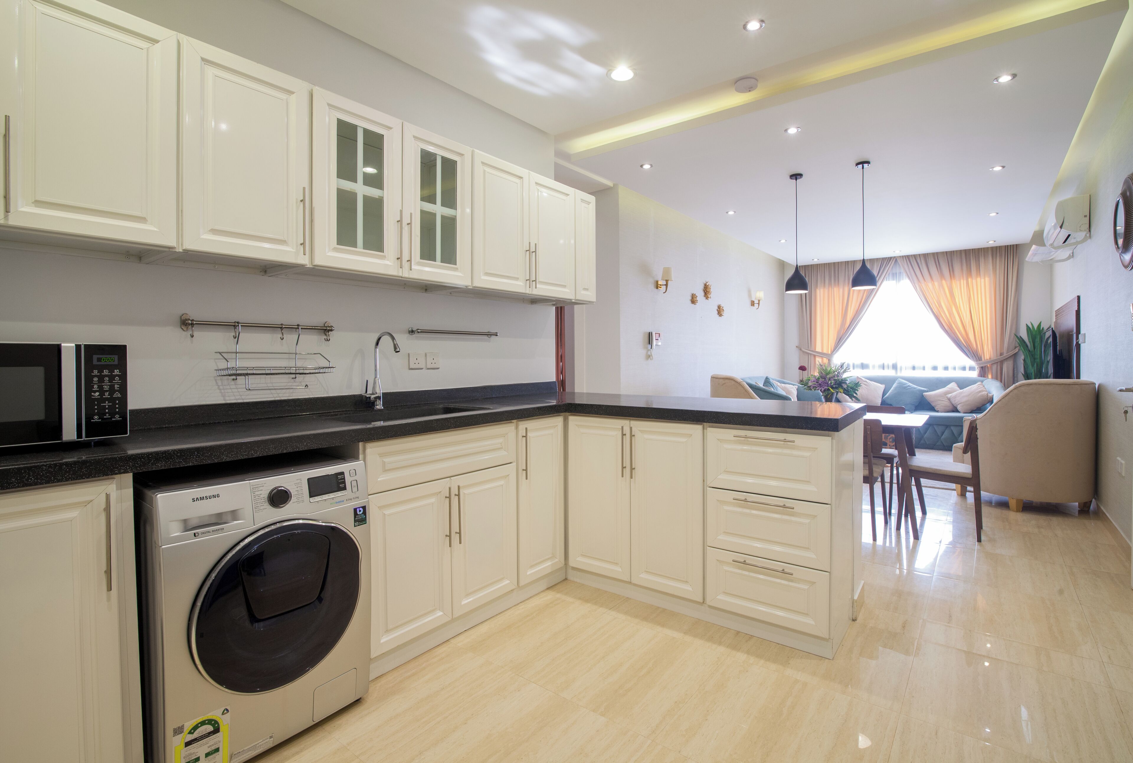 A modern kitchen with white cabinetry, a built-in washing machine, and a dining area with a sofa and table.