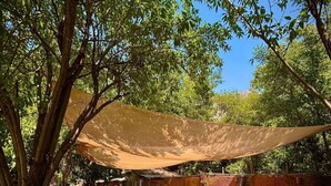 A hammock under a shade sail, outdoor furniture, and a rustic building in a garden setting. - Oceana Suites San San José de Maipo II (San Alfonso)
