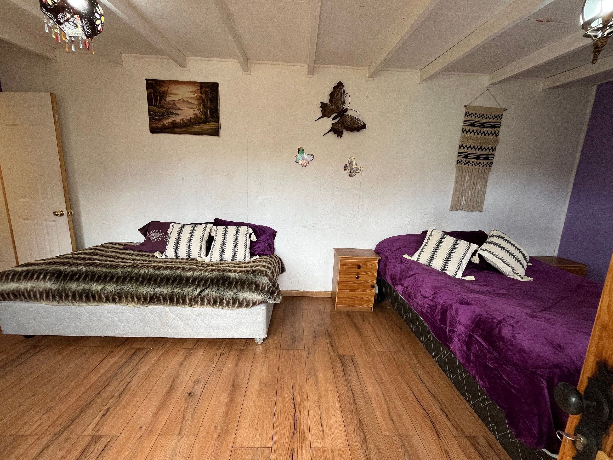 Un dormitorio con cama, mesita de noche, cómoda de madera, un tapiz colgado y un cuadro en la pared.