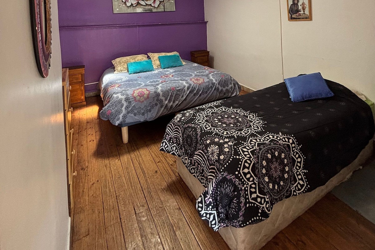 A bedroom with two beds, wooden flooring, a ceiling fan, and a wall-mounted light fixture.