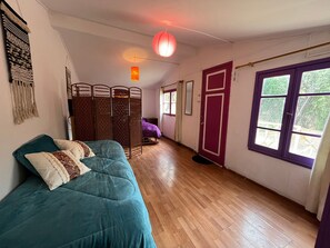 A room with a teal sofa, a wooden floor, a purple door, and a window with a view of greenery.