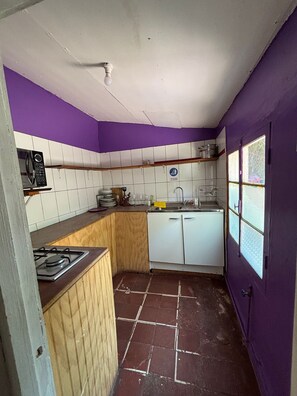 Cocina compacta con estufa a gas, armarios blancos, un lavamanos y una ventana con vistas.