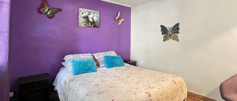 A bedroom with a bed, pillows, a wall-mounted artwork, and a ceiling light fixture.